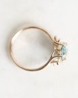 A gold ring with two light blue oval gemstones, photographed from an overhead angle on a light, off-white textured surface.