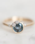 A gold ring featuring a round dark blue gemstone in a bezel setting, accented with small clear stones along the band, photographed on a clean white background.