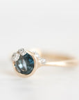 A gold ring featuring a round dark blue gemstone in a bezel setting, accented with small clear stones along the band, photographed on a clean white background.