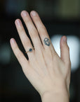A close-up of a person's hand wearing a gold ring with a dark blue gemstone, set against a dark, blurred background.