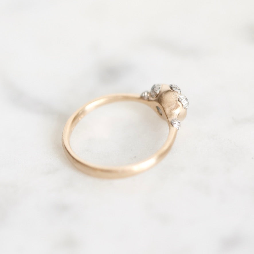 A delicate gold ring with a small cluster of clear gemstones on a polished white marble surface.
