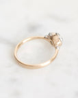 A delicate gold ring with a small cluster of clear gemstones on a polished white marble surface.