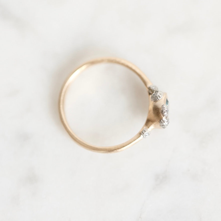 A vintage-style gold ring with a cluster of small silver-colored stones on the band, photographed from above on a white marble surface.