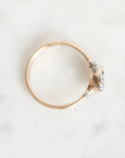 A vintage-style gold ring with a cluster of small silver-colored stones on the band, photographed from above on a white marble surface.