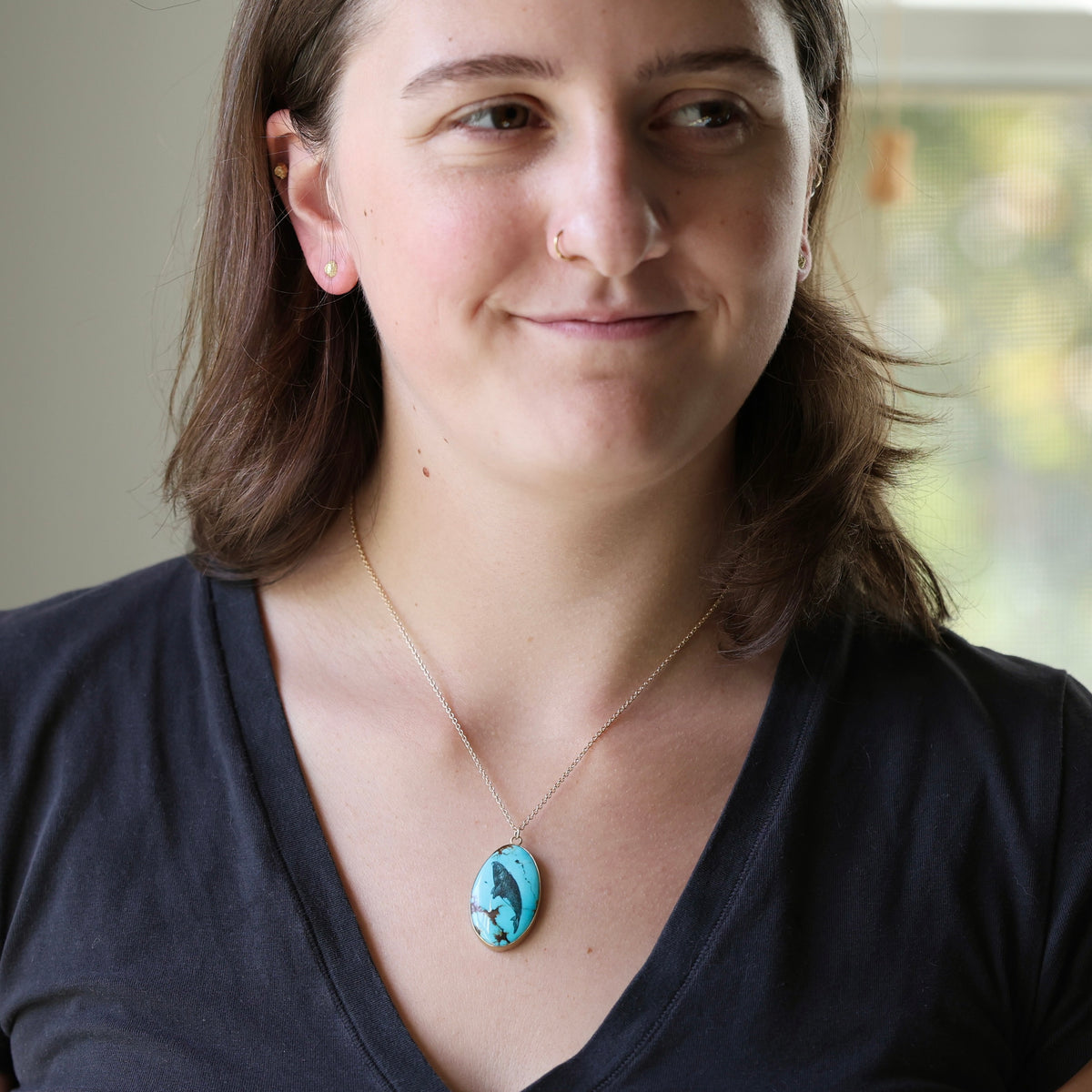 Woman wearing large turquoise pendant with whale engraving in black ink. 