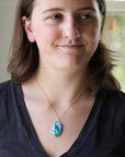 Woman wearing large turquoise pendant with whale engraving in black ink. 
