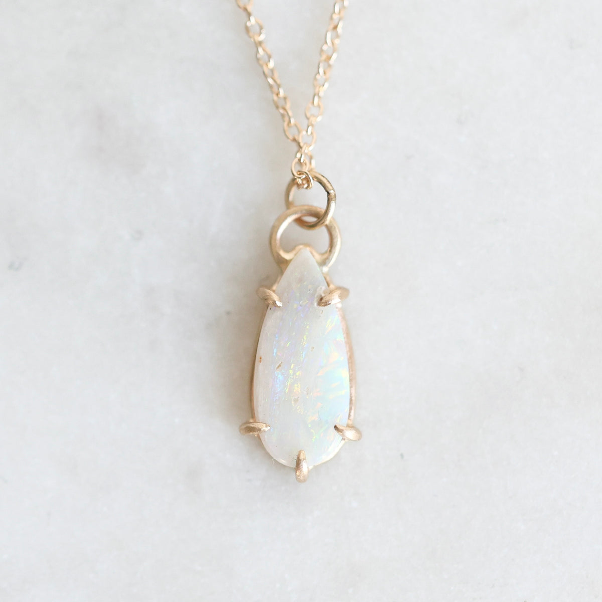 Teardrop opal pendant held in gold prongs against a marble background.