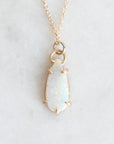 Teardrop opal pendant held in gold prongs against a marble background.