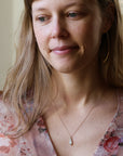 Woman wearing delicate gold chain necklace and floral blouse. She has in large gold hoops. Against a neutral indoor background. 