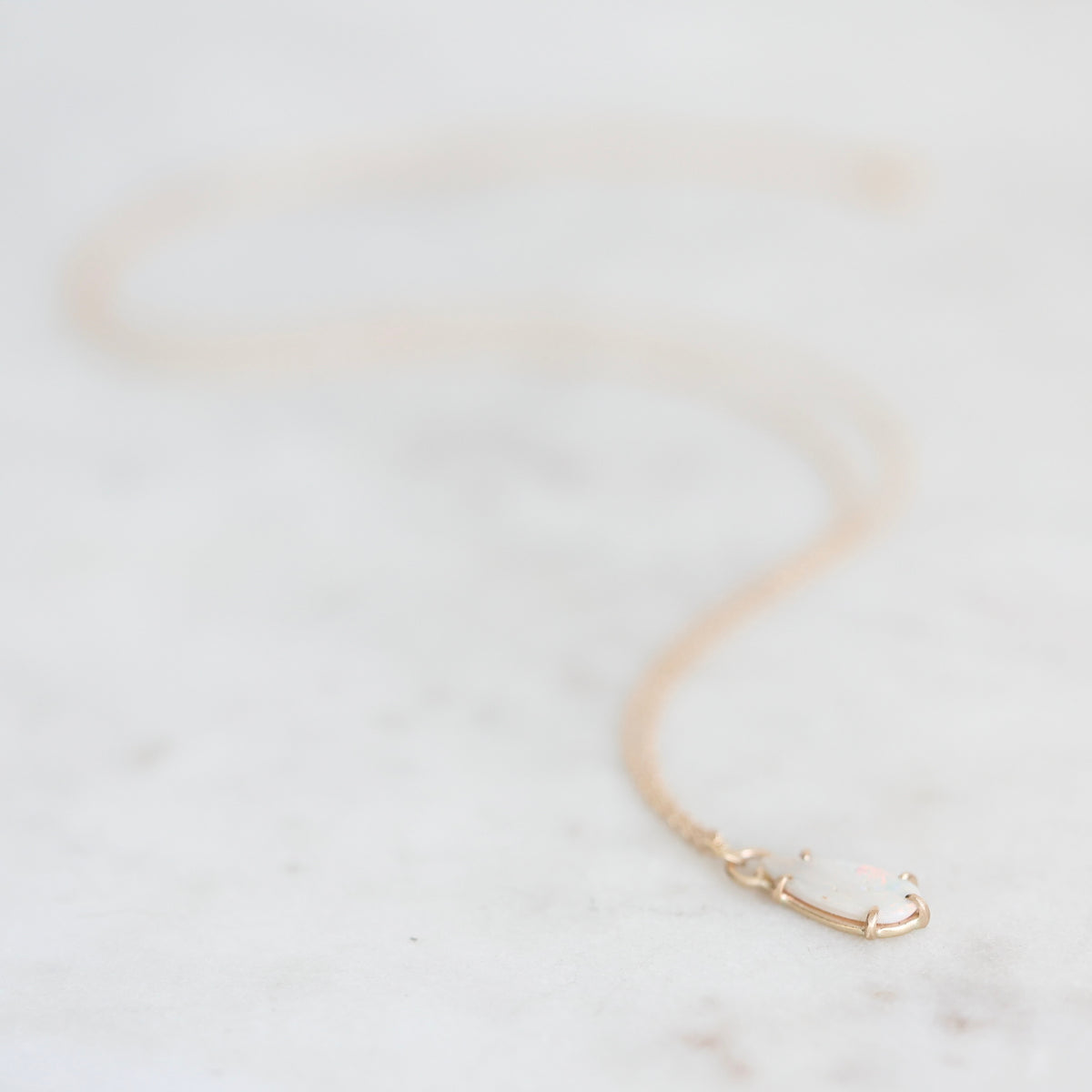 Opal necklace held in gold prongs with a gold chain laying on a marble background. 