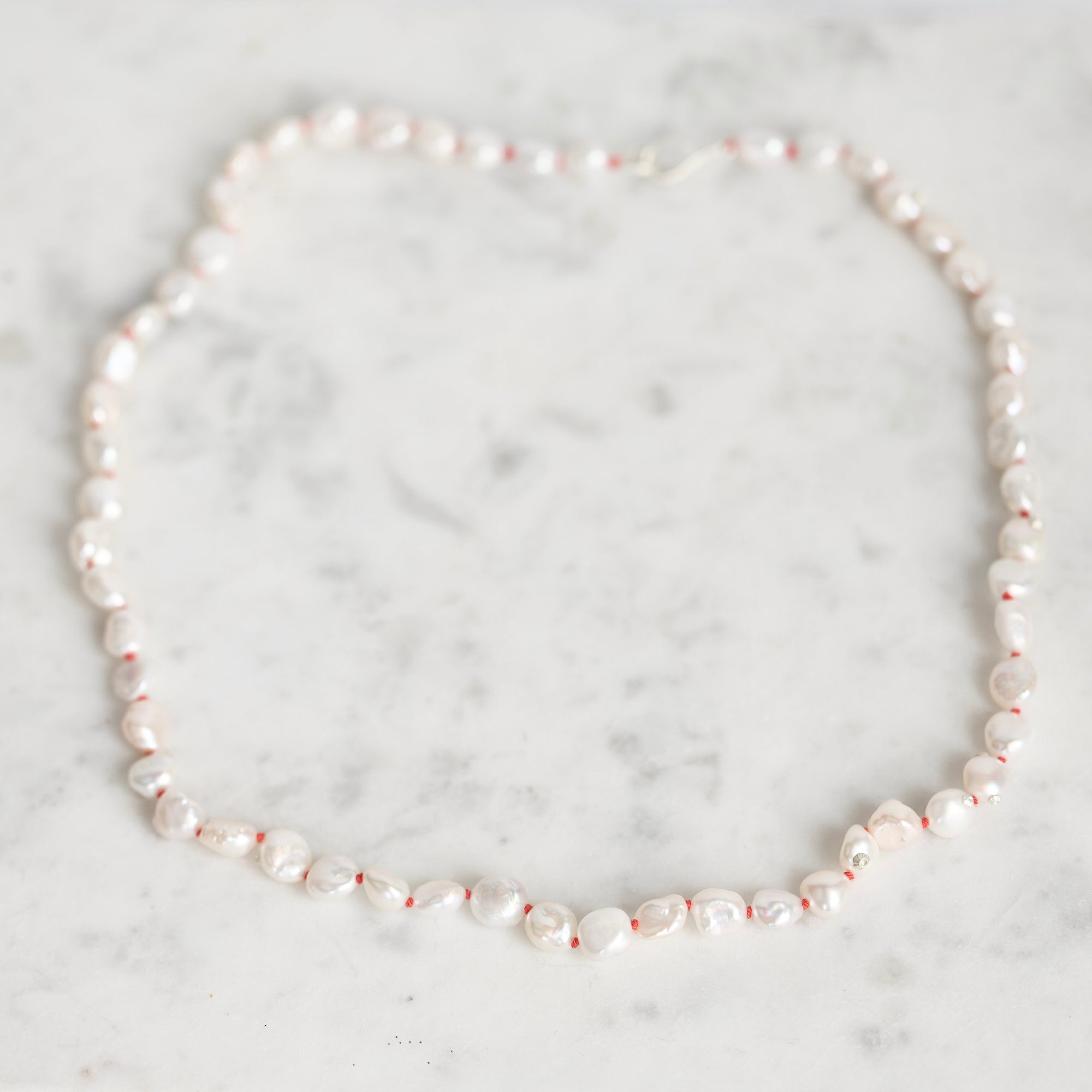 A strand of irregular white baroque pearls laid out in a circle on a light gray and white marble surface.