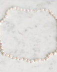 A strand of irregular white baroque pearls laid out in a circle on a light gray and white marble surface.