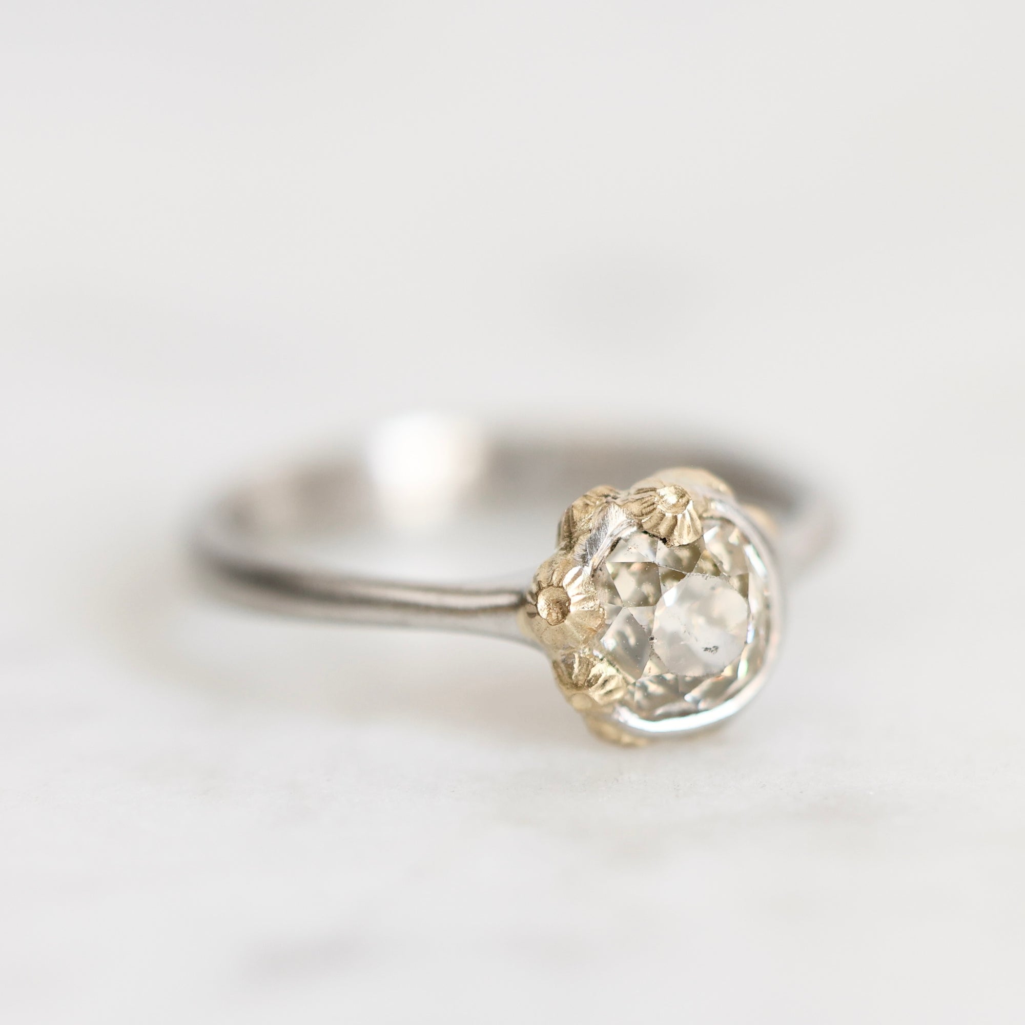 A vintage-style ring featuring a large round clear gemstone in a two-tone setting with a silver band and gold-toned textured accents on the stone.