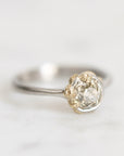 A vintage-style ring featuring a large round clear gemstone in a two-tone setting with a silver band and gold-toned textured accents on the stone.