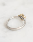 A two-tone ring featuring a polished silver band and a textured, organic-shaped gold top, resting on a light marble surface.