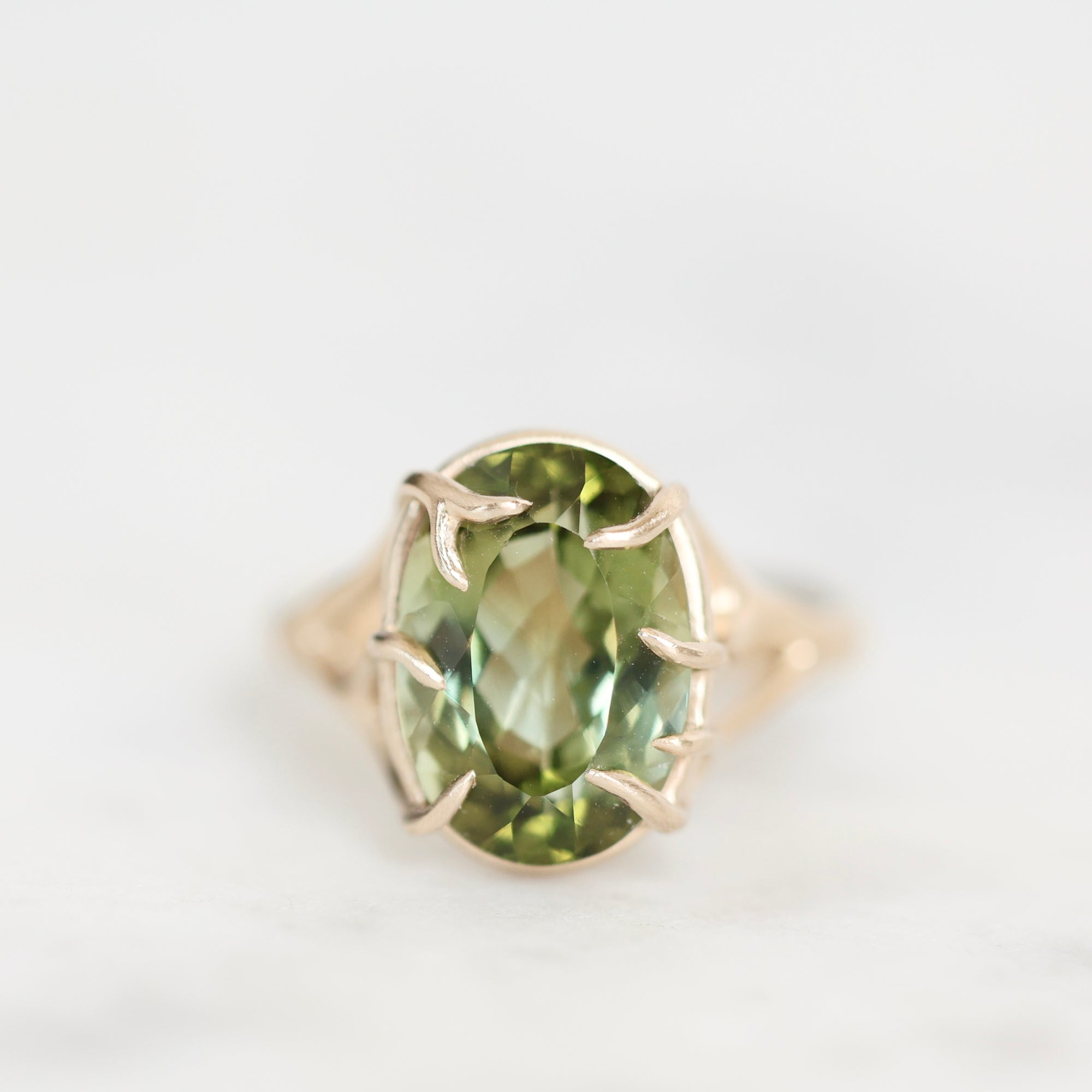 An oval-cut green gemstone ring set in a gold-toned band with a claw-style prong setting, photographed on a clean white background.