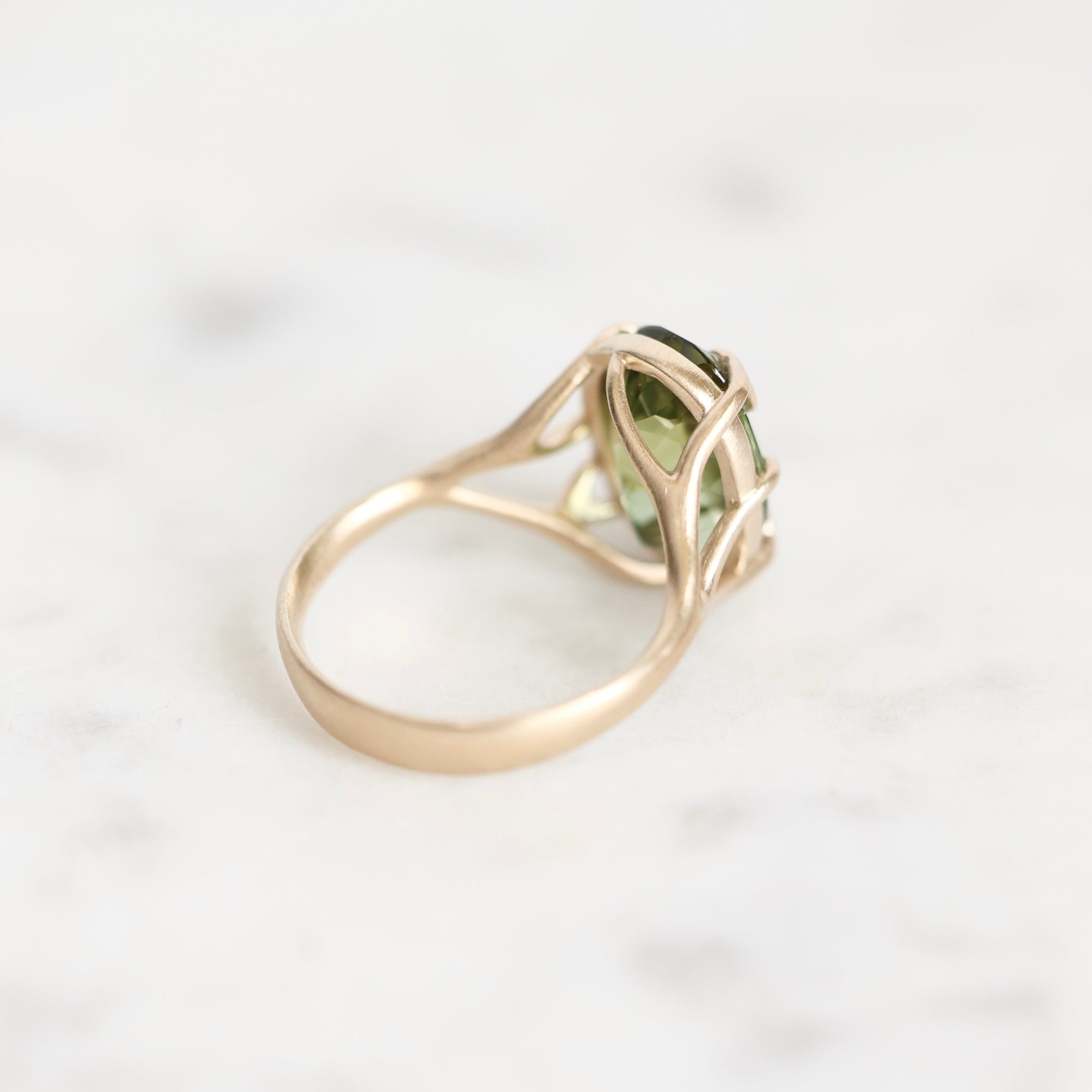 A gold ring with a green gemstone, photographed on a light marble surface.