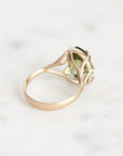 A gold ring with a green gemstone, photographed on a light marble surface.