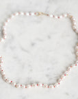 A baroque pearl necklace with small red spacer beads and a gold clasp, displayed on a light gray marble surface.