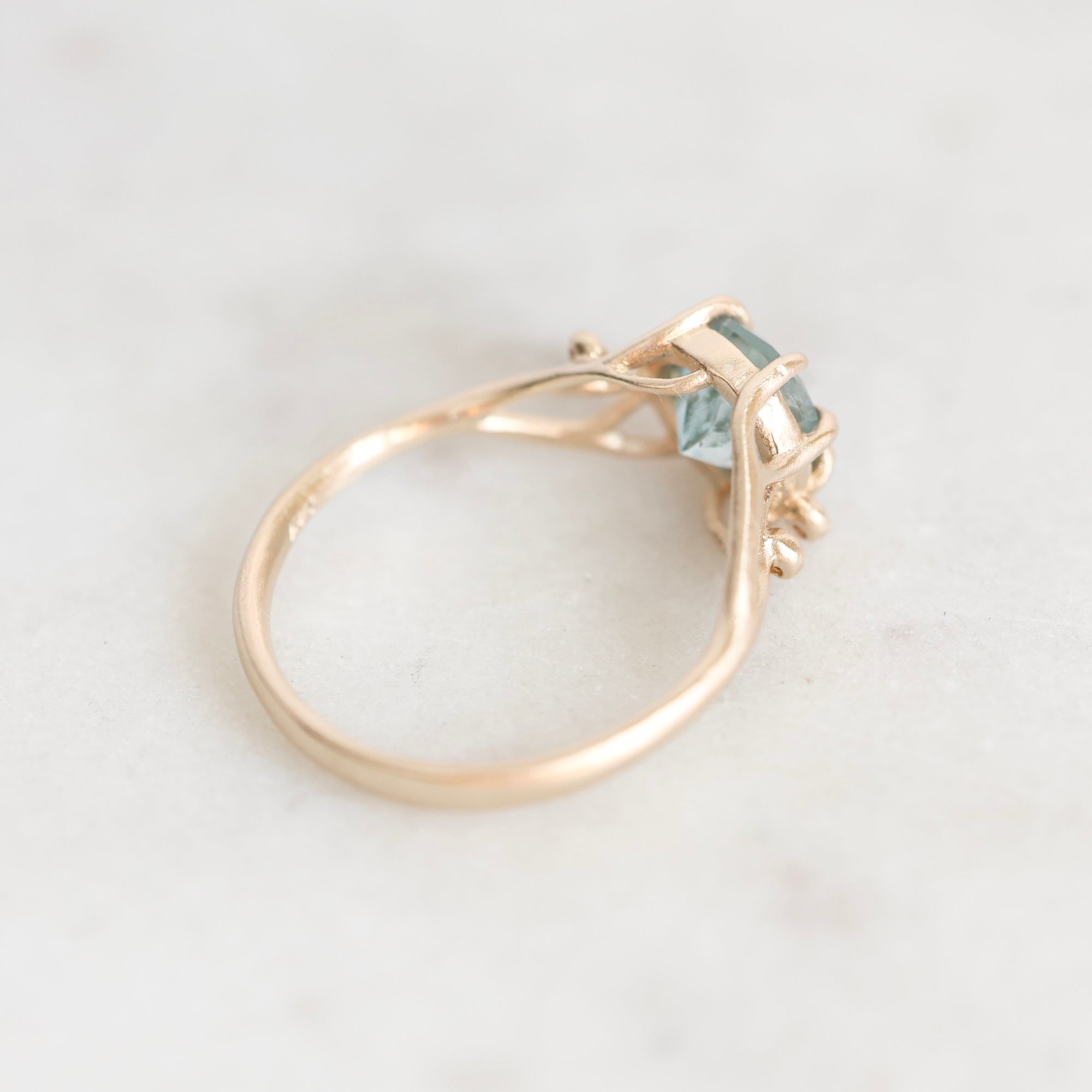 A gold ring with a small light blue gemstone, photographed on a light marble surface.