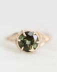 A gold ring featuring a round faceted dark green gemstone held in a prong setting, photographed on a clean white background.
