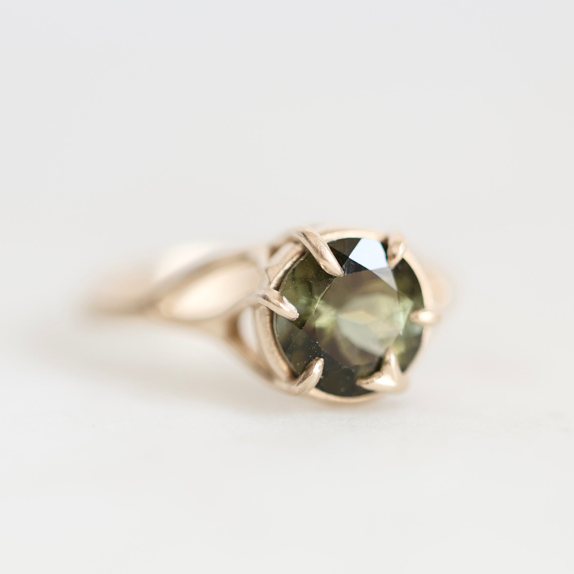 A silver ring featuring a round faceted olive green gemstone in a prong setting, photographed on a clean white background.