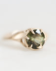 A silver ring featuring a round faceted olive green gemstone in a prong setting, photographed on a clean white background.