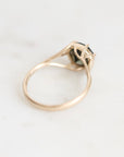 A gold ring with a split shank and a small dark green gemstone, photographed on a light gray marble surface.