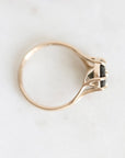 A gold ring with a small black rectangular gemstone in a prong setting, photographed from above on a light off-white background.