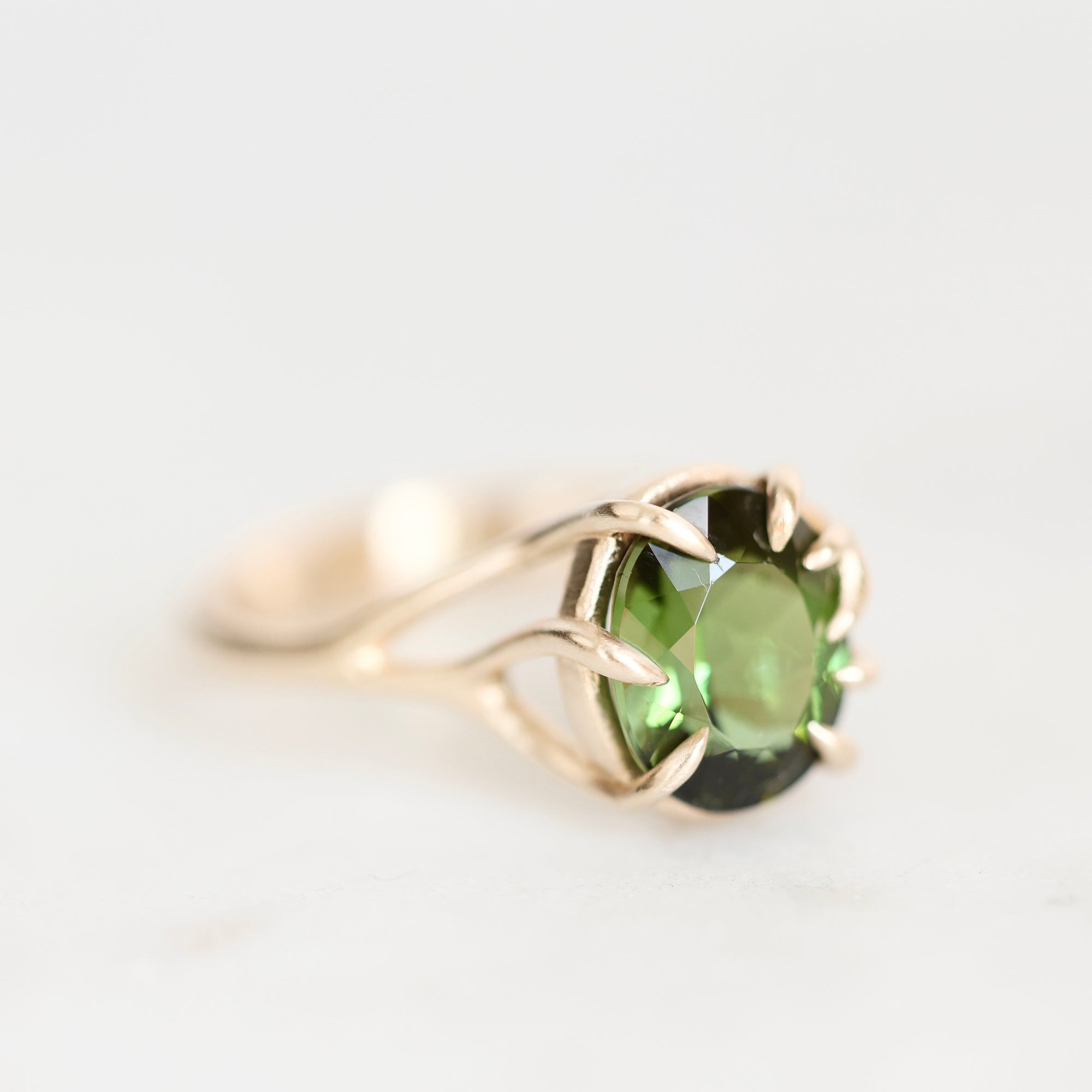 A gold ring featuring a round green gemstone in a prong setting, photographed on a clean white background.