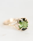 A gold ring featuring a round green gemstone in a prong setting, photographed on a clean white background.