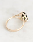 A gold ring with a green gemstone in a split-prong setting, photographed on a light marble surface.
