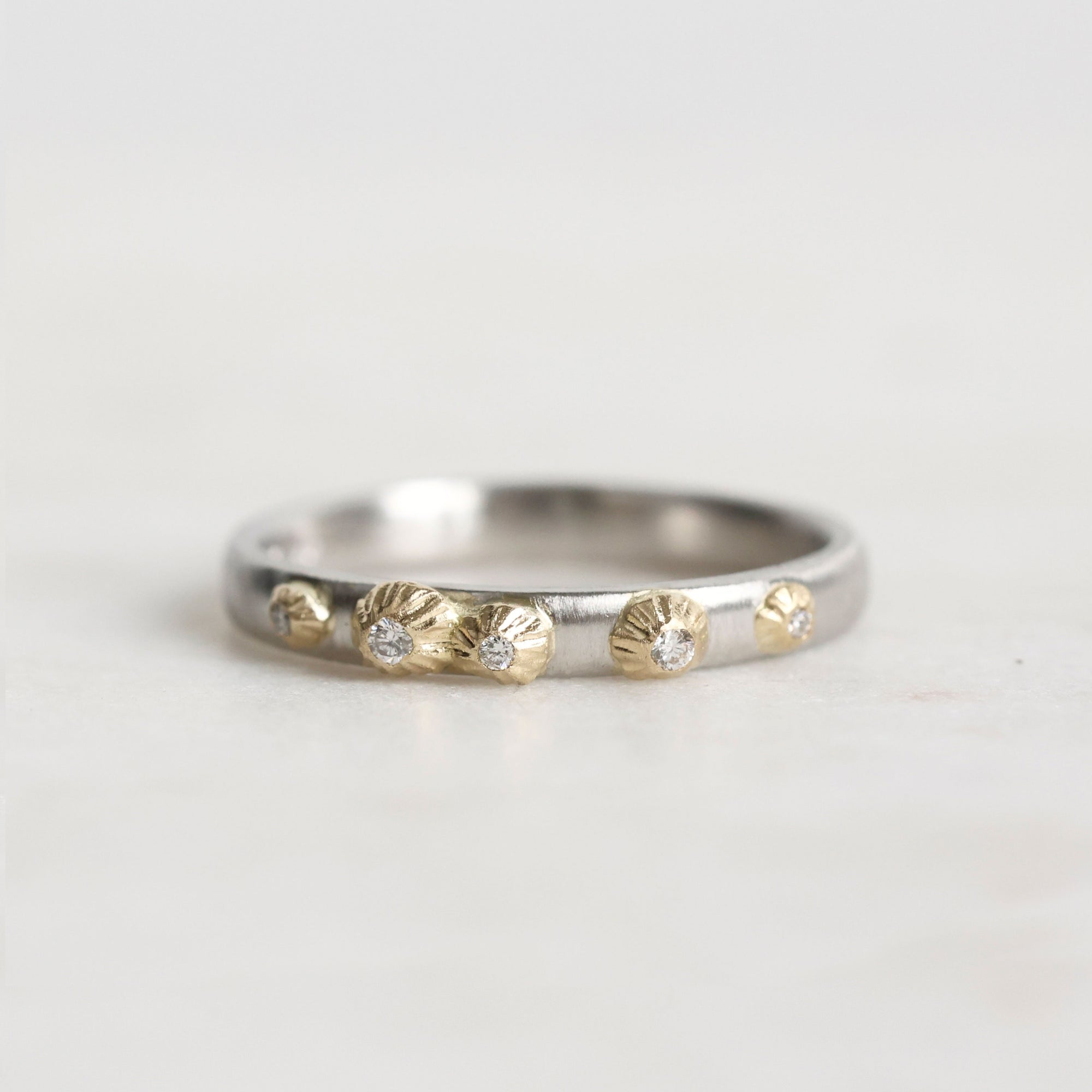 Silver ring with gold accents and small stones on a light gray background