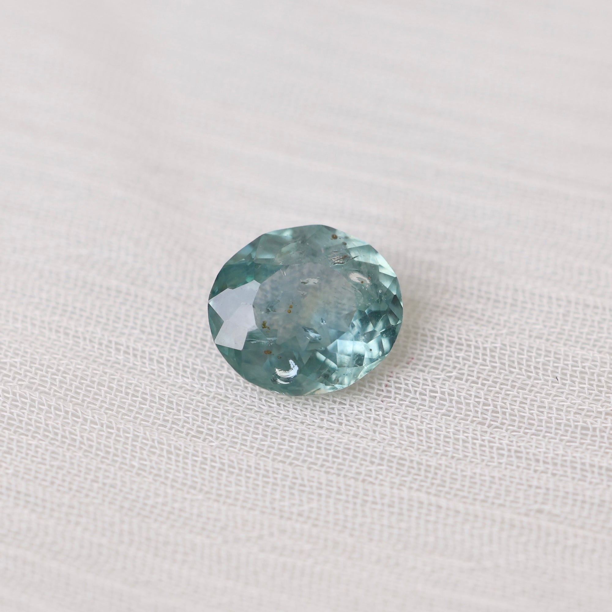 Greenish-blue gemstone on a white fabric background