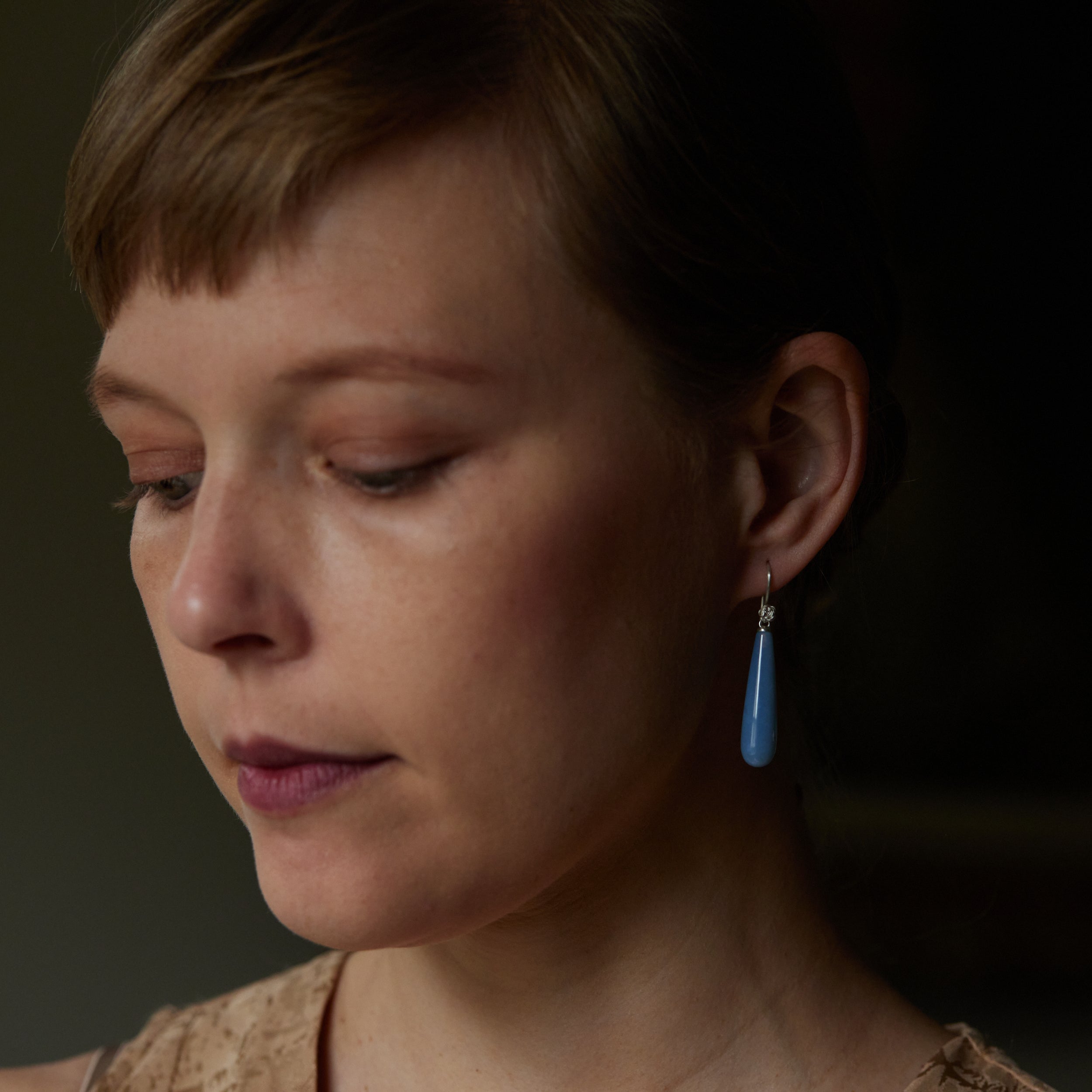 long teardrops of blue common opal hang beneath silver ear wires and roses. Shown on person.
