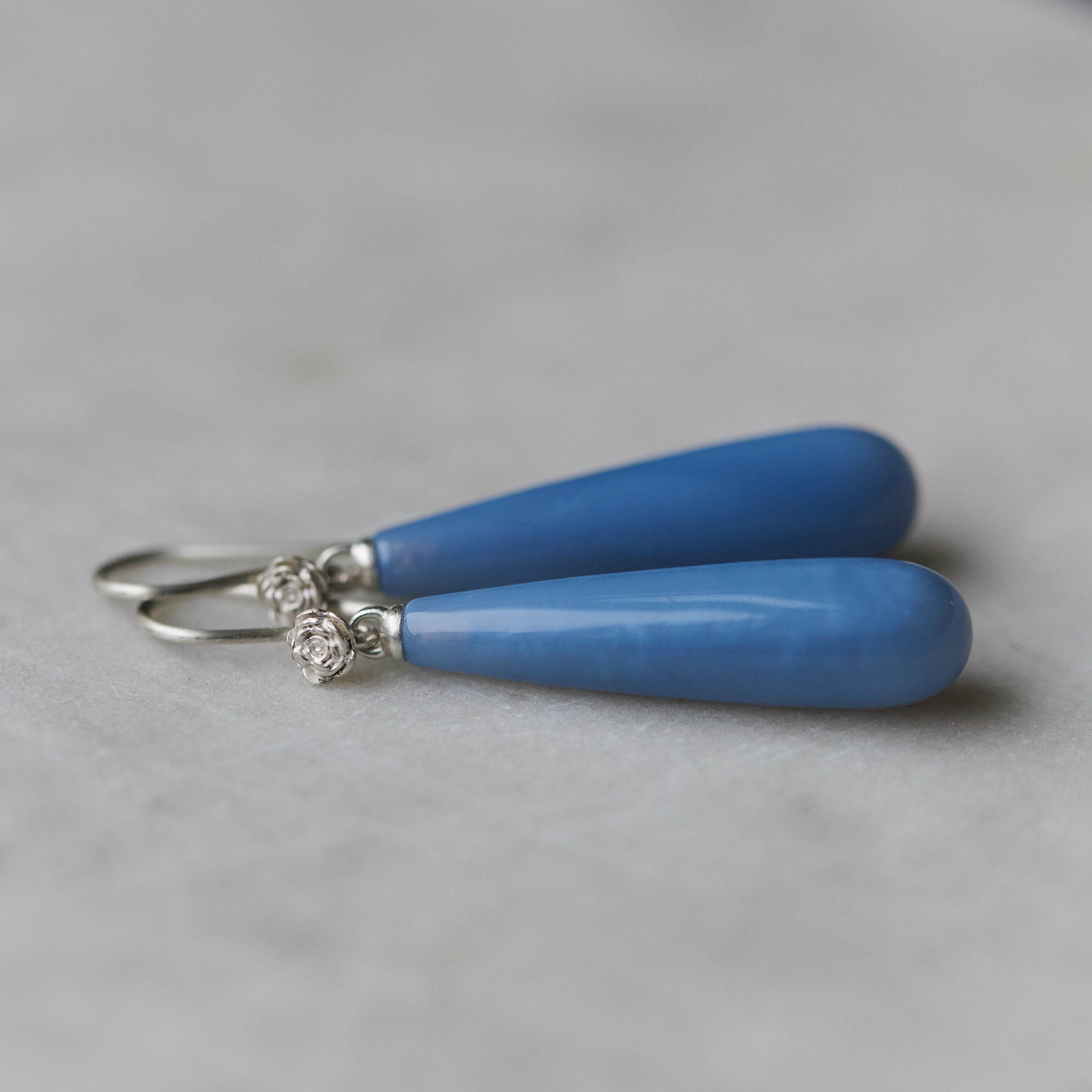long teardrops of blue common opal hang beneath silver ear wires and roses