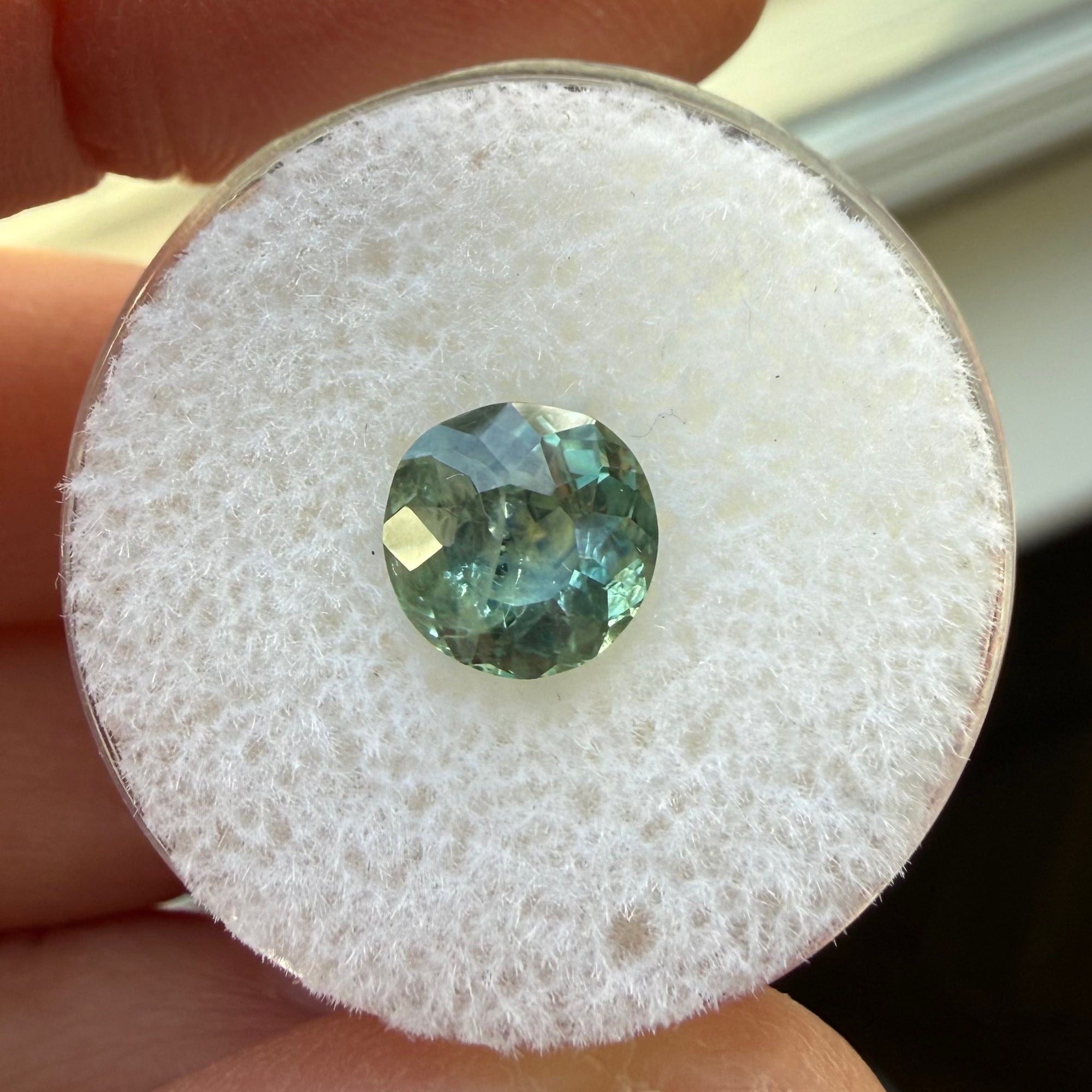 Green gemstone on a white cushion with a hand holding it