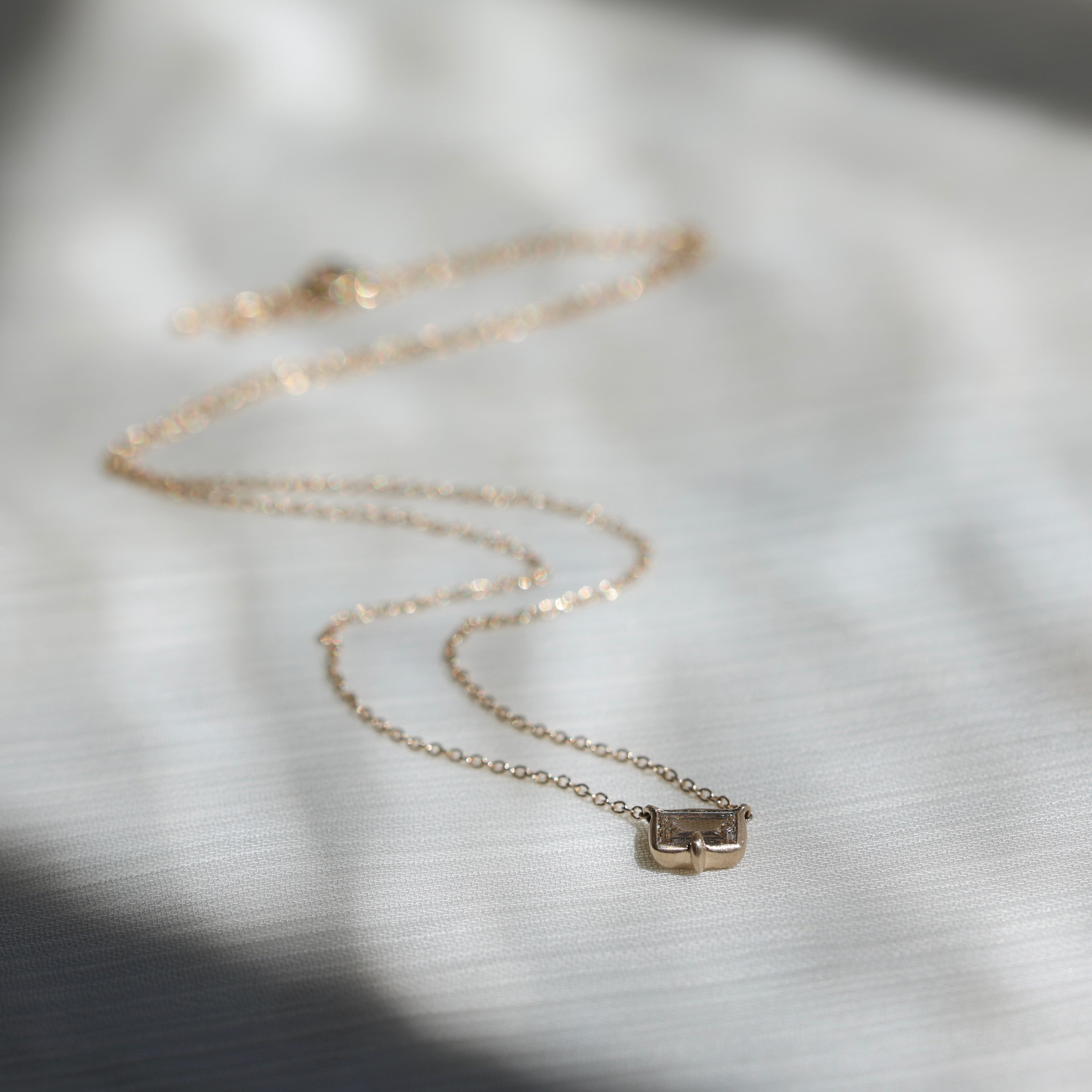 Gold necklace with a small diamond pendant on a light fabric background