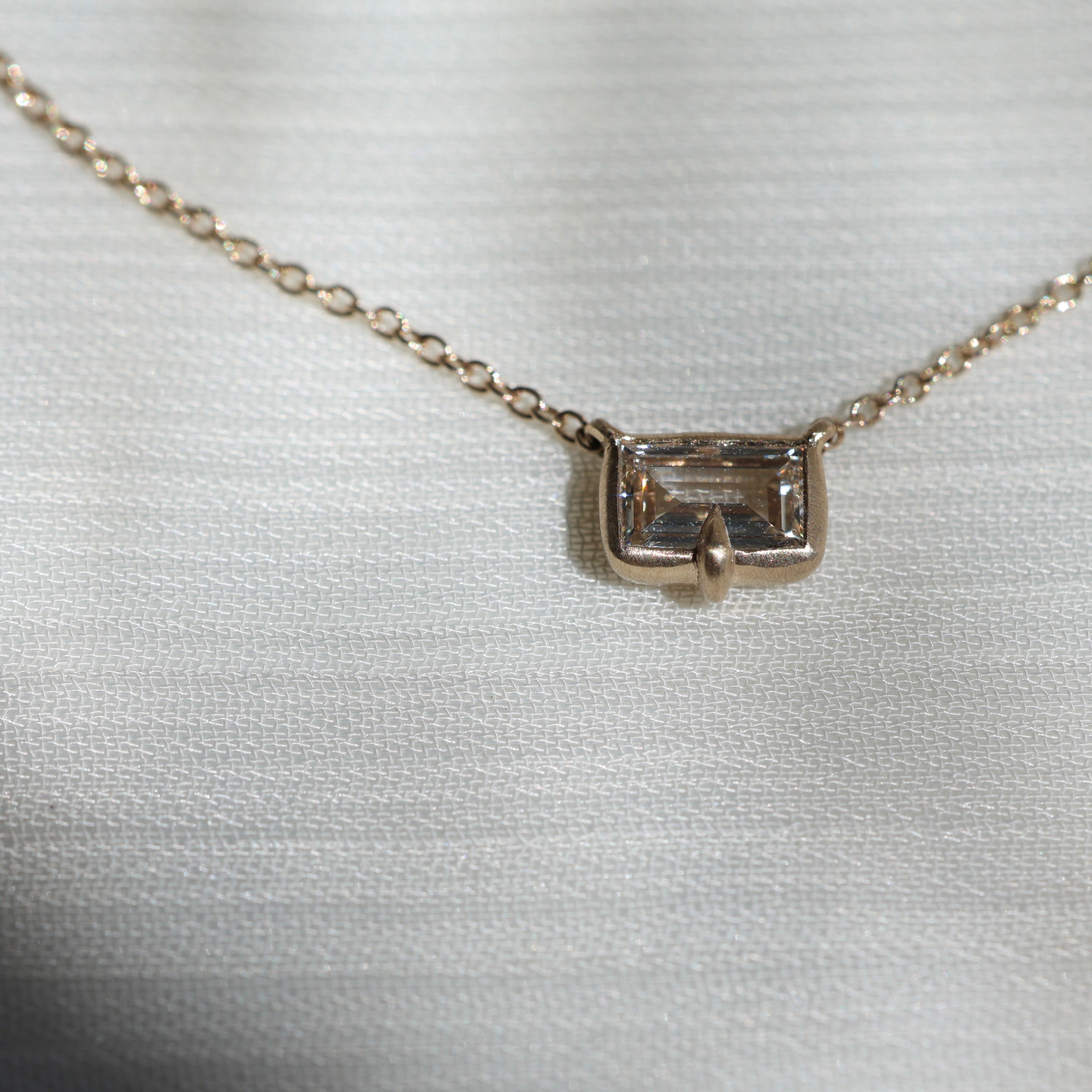 Gold necklace with a small diamond pendant on a light fabric background