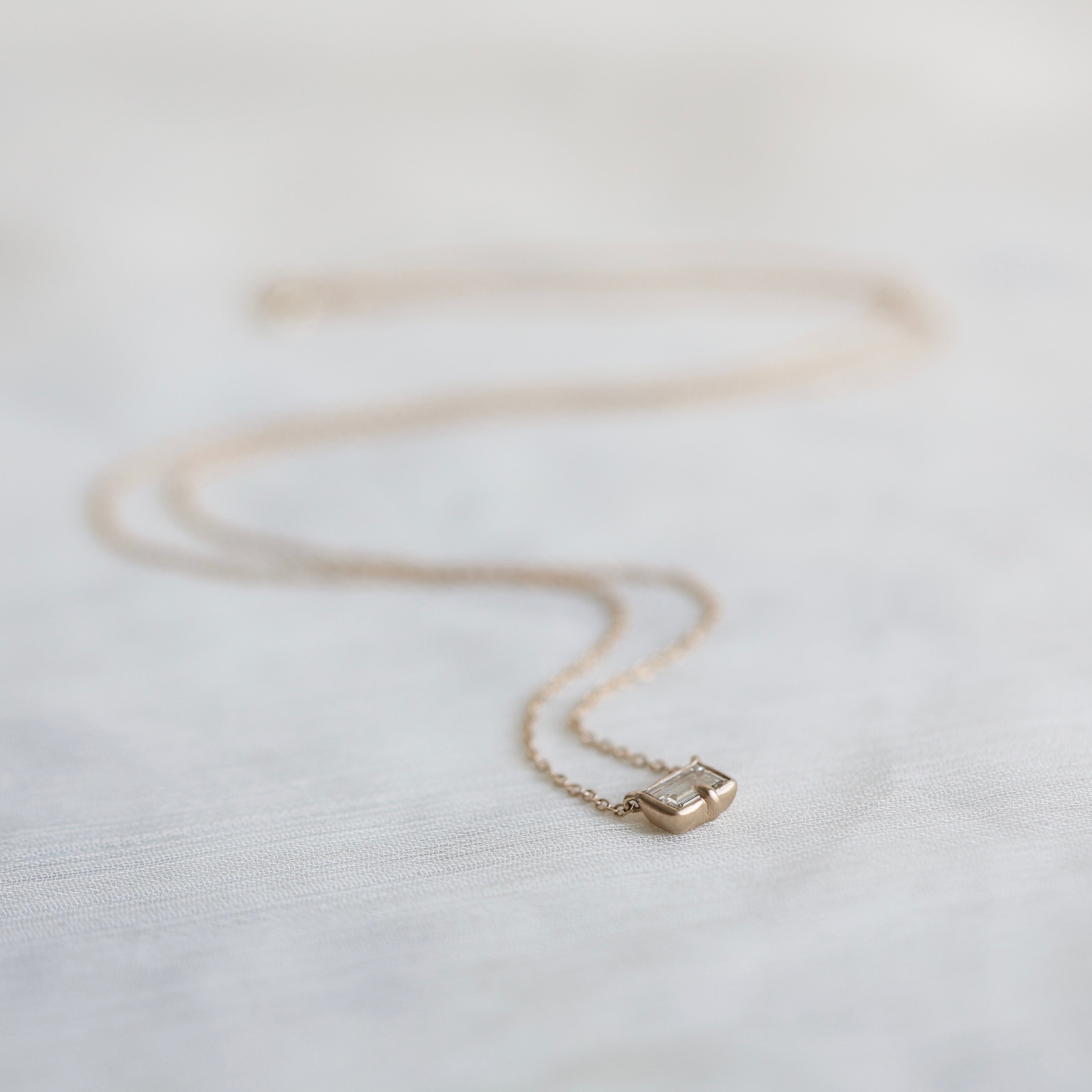 Gold necklace with a small diamond pendant on a light fabric background