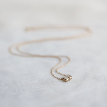 Gold necklace with a small diamond pendant on a light fabric background