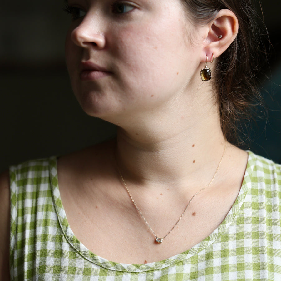 Close-up of a person wearing earrings and a necklace with a green and white checkered top.