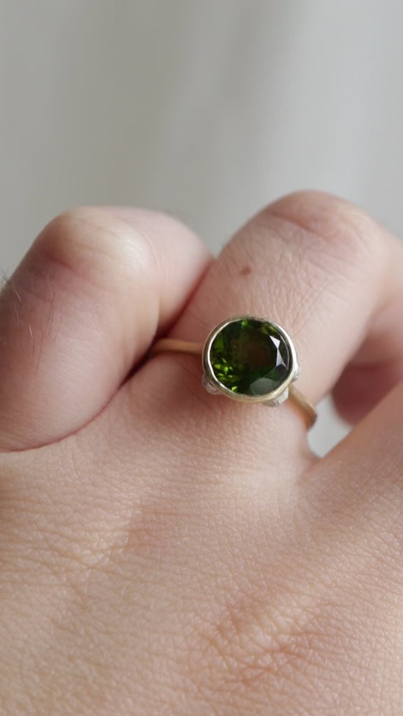 Video of 14k yellow gold bezel set ring with a green Tourmaline and bright sterling silver barnacles against a neutral background, displayed on ring finger.