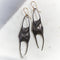 A pair of sculptural dangle earrings with dark oxidized metal bodies and gold-tone hook ear wires, resting on a light marble surface.