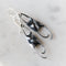 A pair of sculptural dangle earrings with organic, flowing shapes in bright silver and dark oxidized black, resting on a light marble surface.