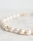A close-up of a pearl strand necklace resting on a light marble surface. The pearls are white with subtle luster and photographed against a soft, out-of-focus light background