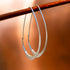 Large Facet Hoops in silver hanging from a wood stick, set against an orange background- Hannah Blount Jewelry